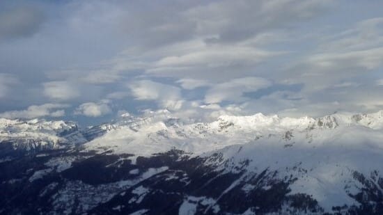 Vaste chaîne de montagnes enneigées sous un ciel partiellement nuageux.