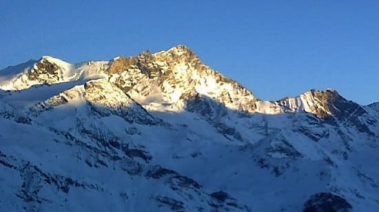Vue des montagnes Bishorn, Weisshorn et Schalihorn illuminées par les derniers rayons de soleil au crépuscule, avec un ciel bleu clair.
