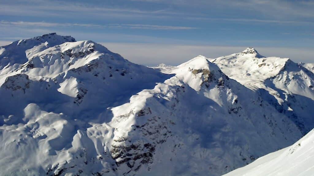Vue panoramique des montagnes enneigées, avec le Sasseneire au premier plan et la Pointe de Lona en arrière-plan, sous un ciel partiellement nuageux.
