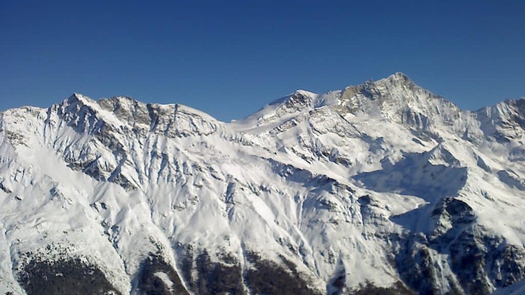 Vue des montagnes enneigées, incluant le Sasseneire et la Pointe de Lona, avec un ciel bleu clair.