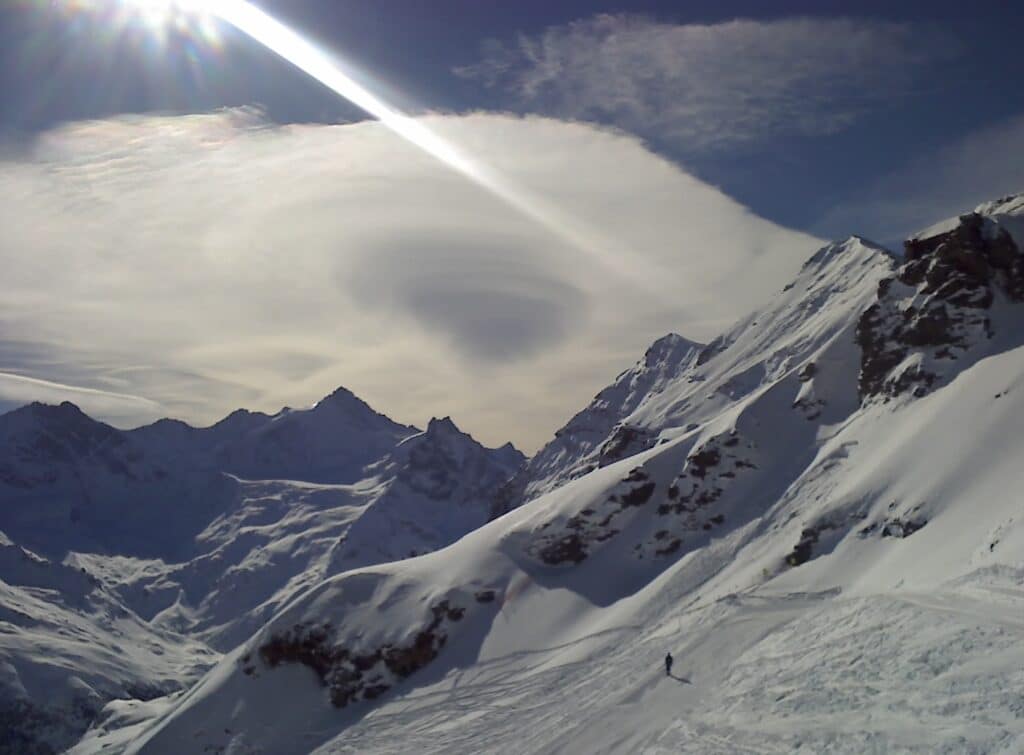 Vue de montagnes enneigées avec un ciel et un nuage en forme d'entonnoir, capturée lors des conditions hivernales.