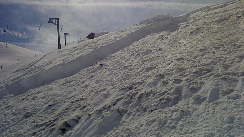 Vue de la pente de neige avec des équipements de ski en arrière-plan. La neige est tassée, montrant des traces de glissement sur la surface.