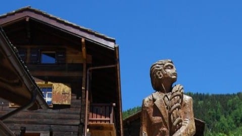 Sculpture en bois et chalet traditionnel sous un ciel bleu clair.