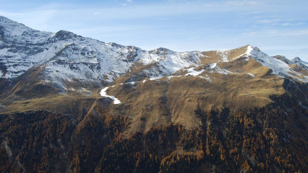 Vue panoramique des montagnes de Sorebois avec des restes de neige sur les versants nord, entourées de forêts dorées en automne.