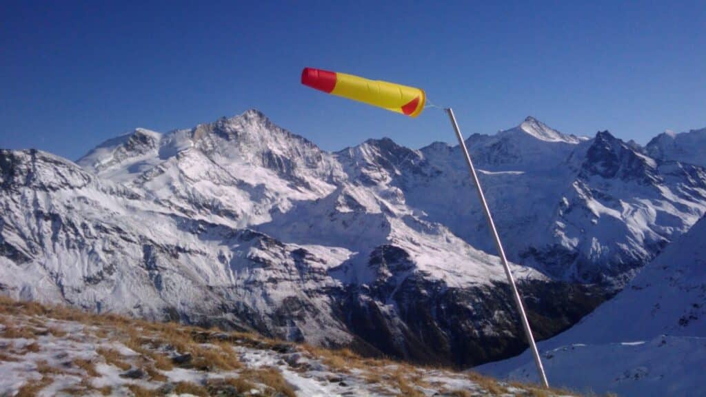 Vue des montagnes enneigées avec une manche à air jaune et rouge au premier plan, indiquant la direction du vent.