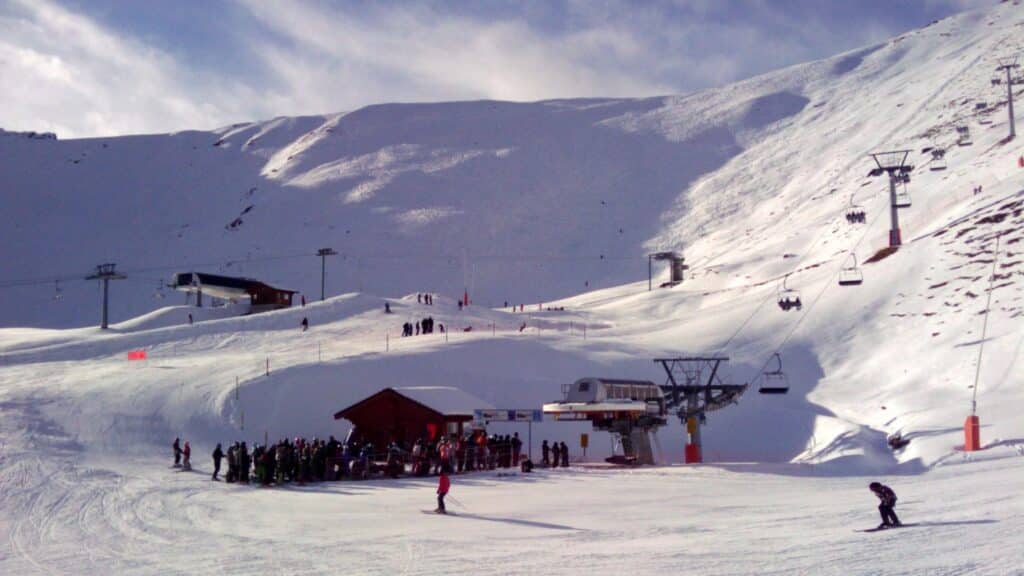 Station de ski avec neige fraîche, télésièges et skieurs sur la piste, montagnes en arrière-plan.