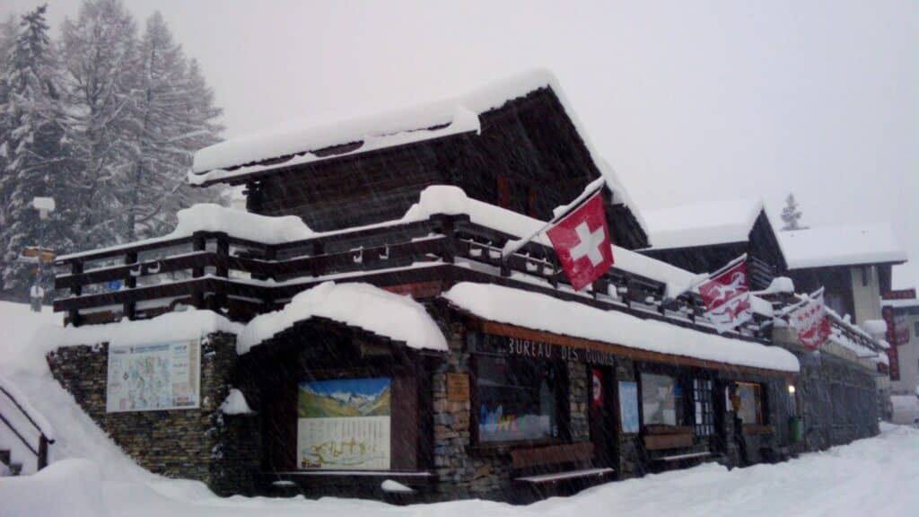 A snow-covered building with Swiss flags, surrounded by trees in a winter setting.
