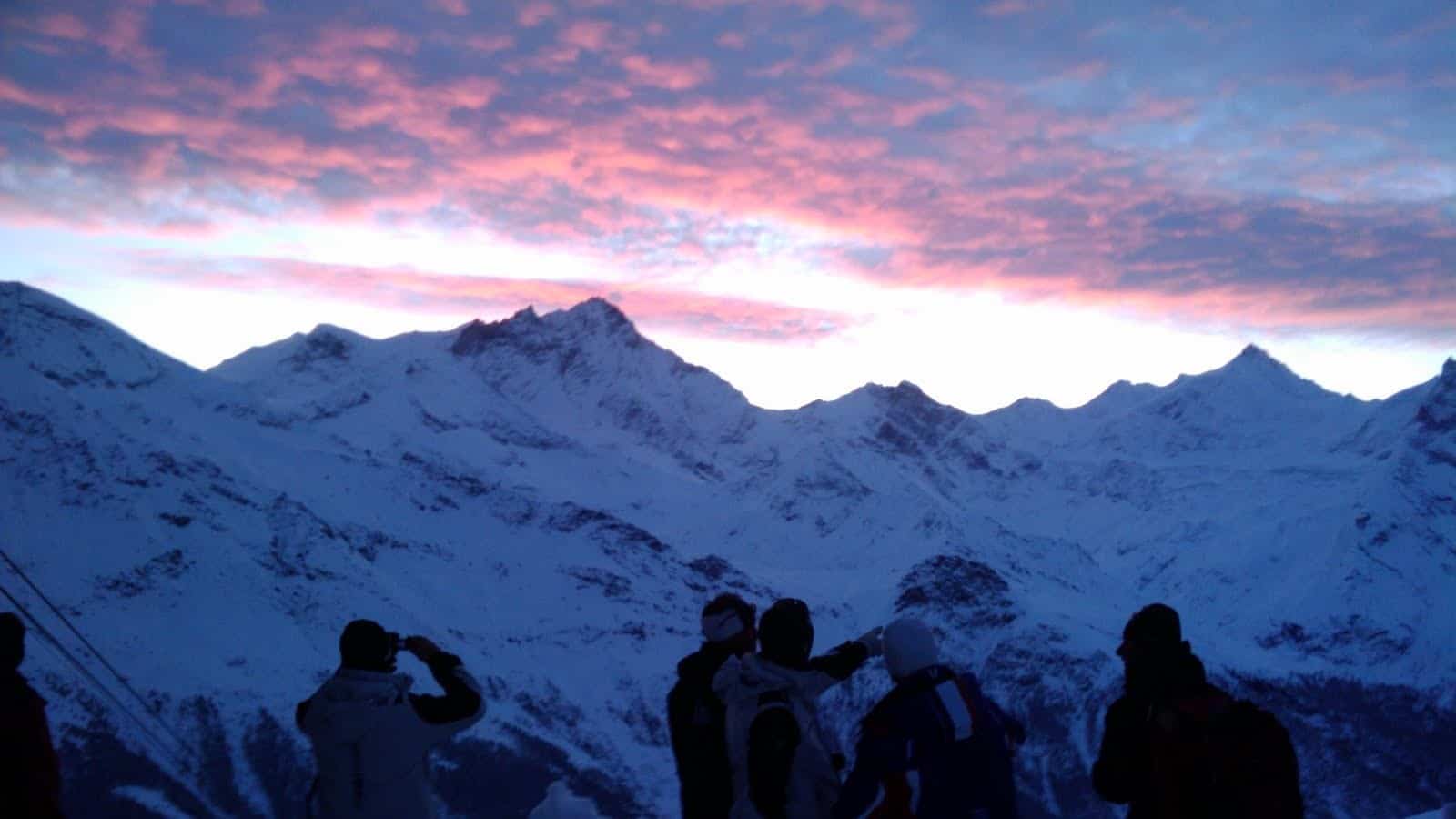 Coucher de soleil rose sur montagnes enneigées avec skieurs.