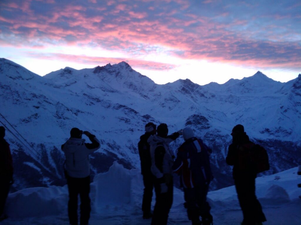 Des skieurs admirent le lever du soleil sur les montagnes enneigées, avec des nuages altocumulus colorés au-dessus du Weisshorn.