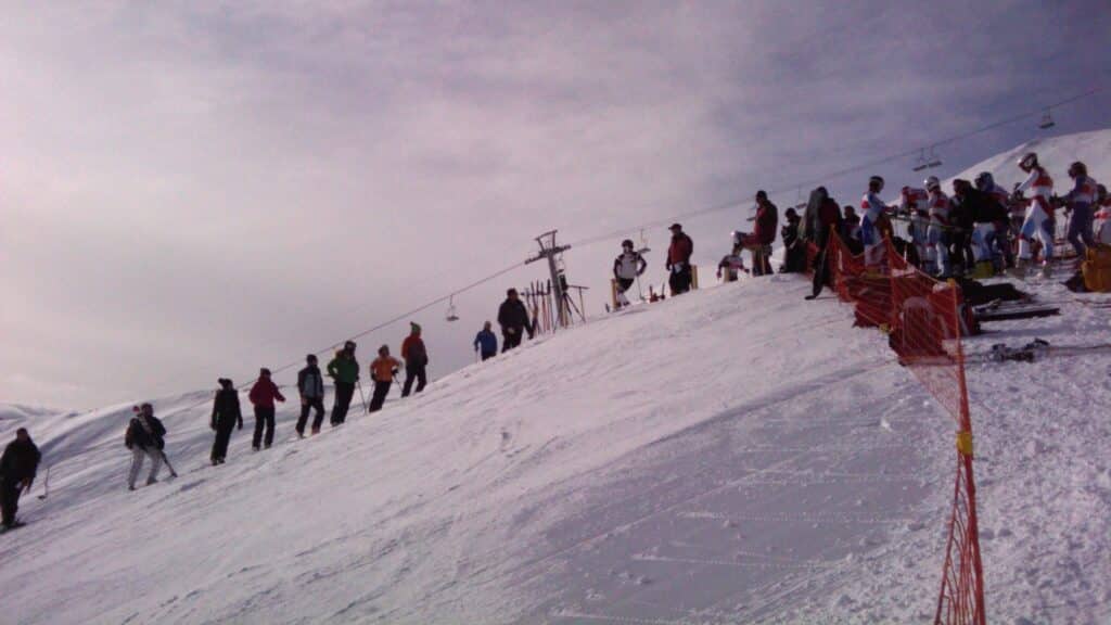 Des skieurs attendent au sommet d'une piste enneigée pendant une course de slalom géant.