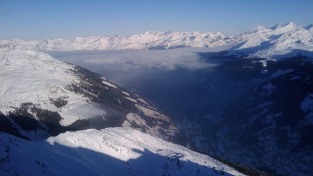 Vue panoramique sur un paysage montagneux couvert de neige, avec des sommets enneigés sous un ciel bleu dégagé, témoignant de conditions de ski idéales.
