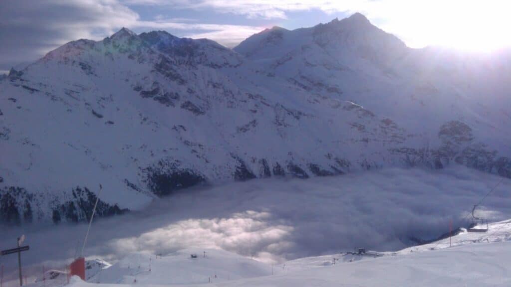 Vue panoramique sur les montagnes enneigées de Zinal avec des nuages dans la vallée en dessous.