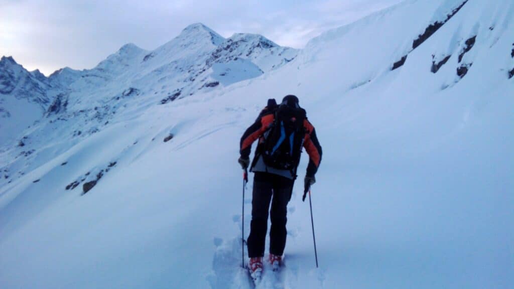 Un skieur s'aventure à travers une neige fraîche en montagne, avec des sommets enneigés en arrière-plan.