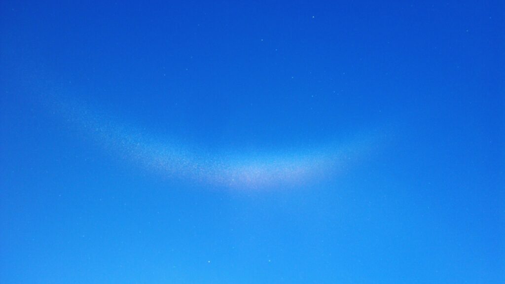 Un ciel bleu avec une légère courbe de cristaux de glace apportant des reflets colorés, capturant la lumière du soleil.