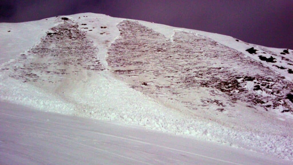 Image montrant un versant de montagne recouvert de neige, avec des traces visibles d'avalanches récentes sur la pente.