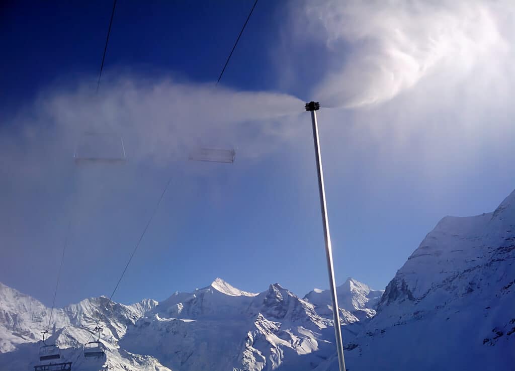 Un canon à neige Saphir fonctionnant avec les montagnes enneigées en arrière-plan, sous un ciel bleu.