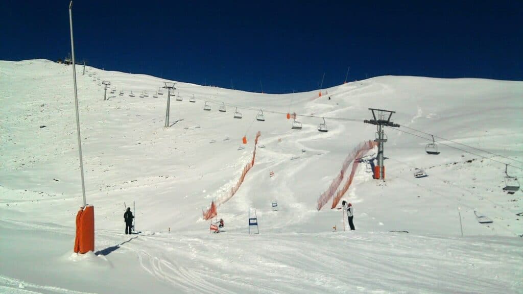 Vue d'une station de ski avec des pistes enneigées, des remontées mécaniques et un ciel bleu dégagé.