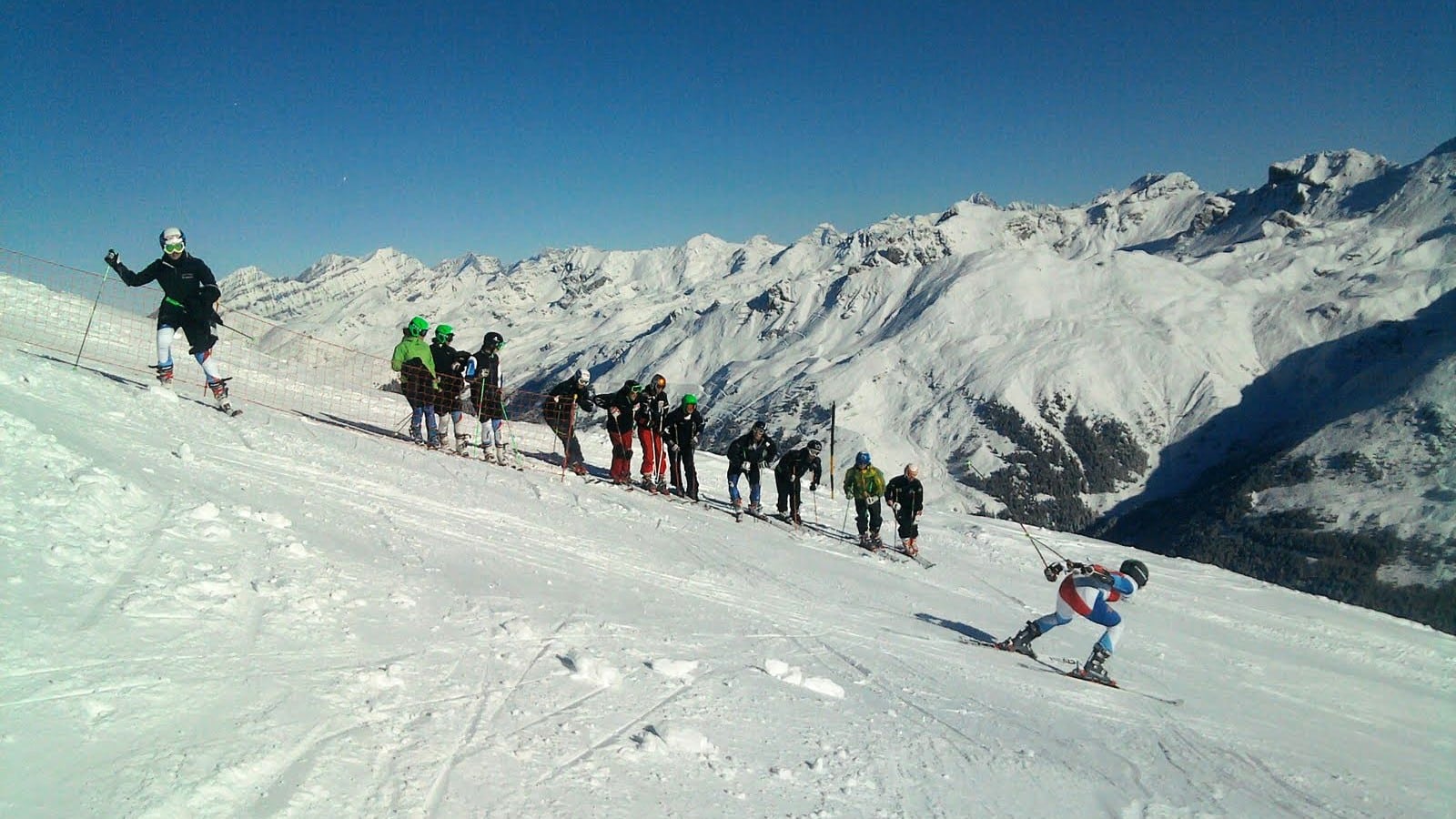 Skieurs sur piste, montagnes enneigées sous un ciel bleu éclatant.