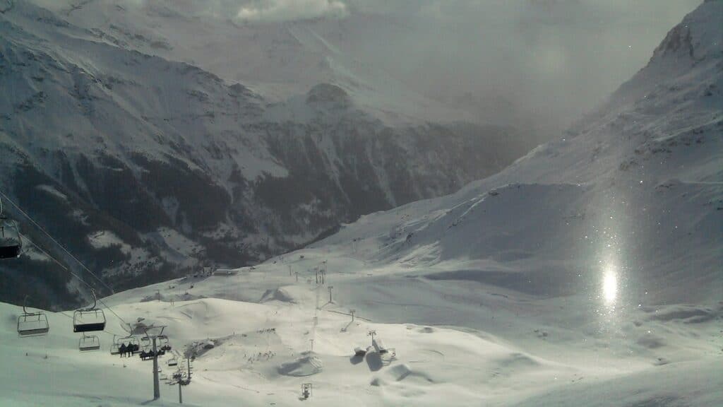 Paysage montagneux enneigé avec des pistes de ski et des remontées mécaniques sous un ciel nuageux