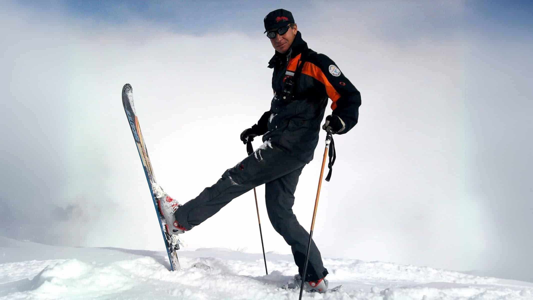 Skieur avec un ski levé posant sur une montagne enneigée.