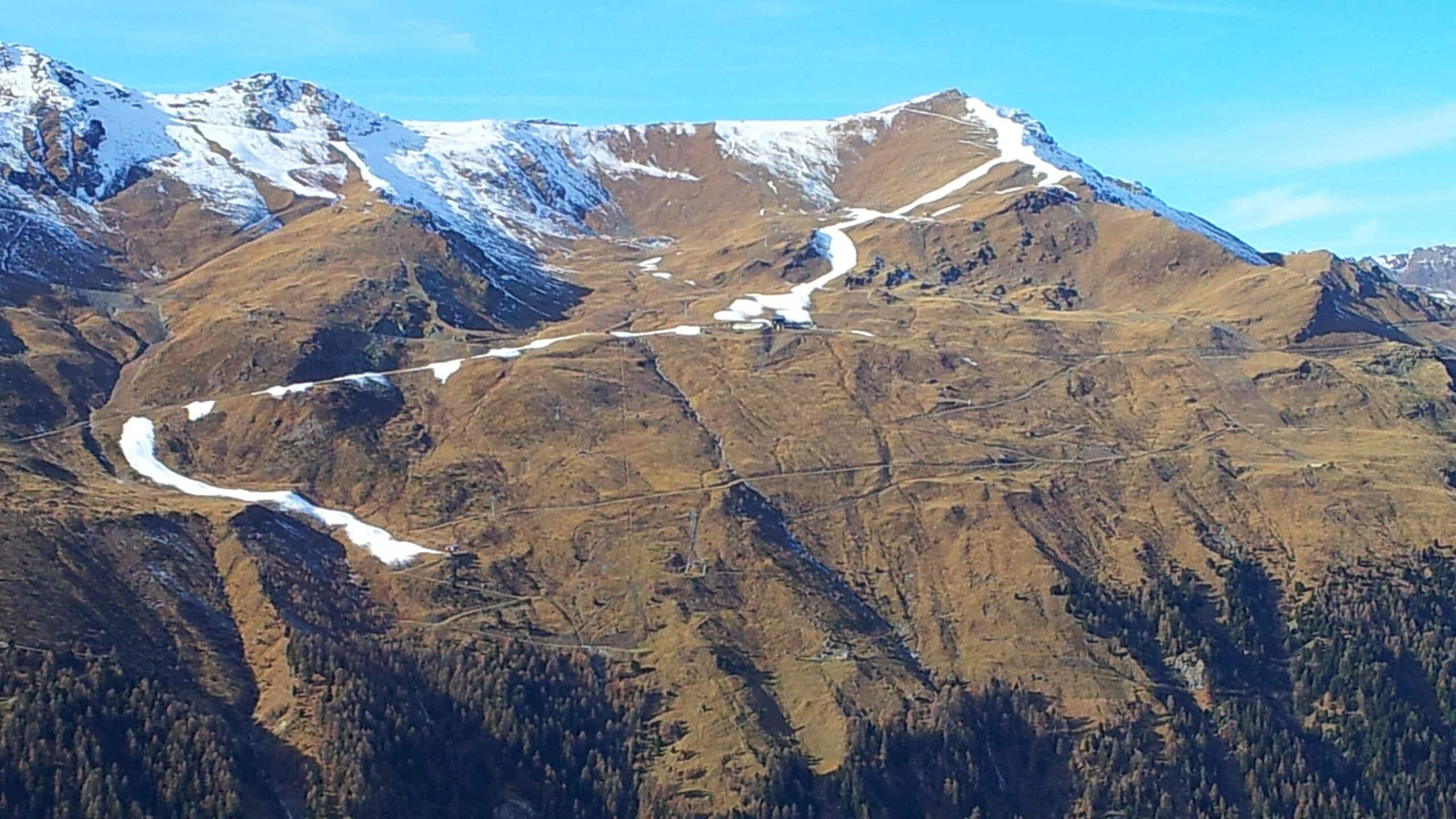 Montagnes enneigées avec pentes brunes et forêt sous ciel bleu.