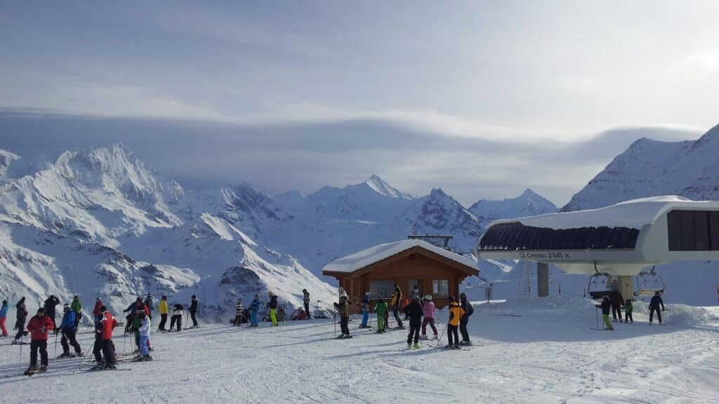 Groupe de skieurs au sommet d'une station de ski avec des montagnes enneigées en arrière-plan et une remontée mécanique.