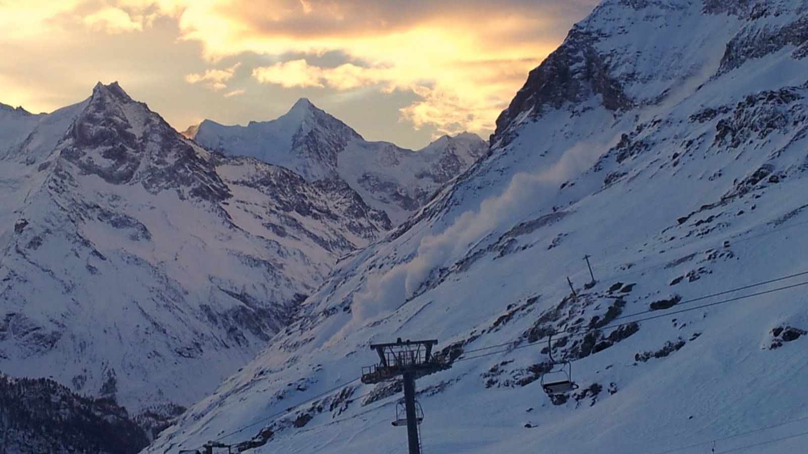 Paysage montagneux enneigé avec avalanche et télésiège sous ciel coloré.