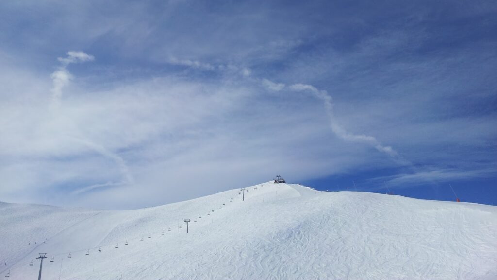 Vue d'une montagne enneigée sous un ciel bleu, avec des remontées mécaniques visibles sur la pente.