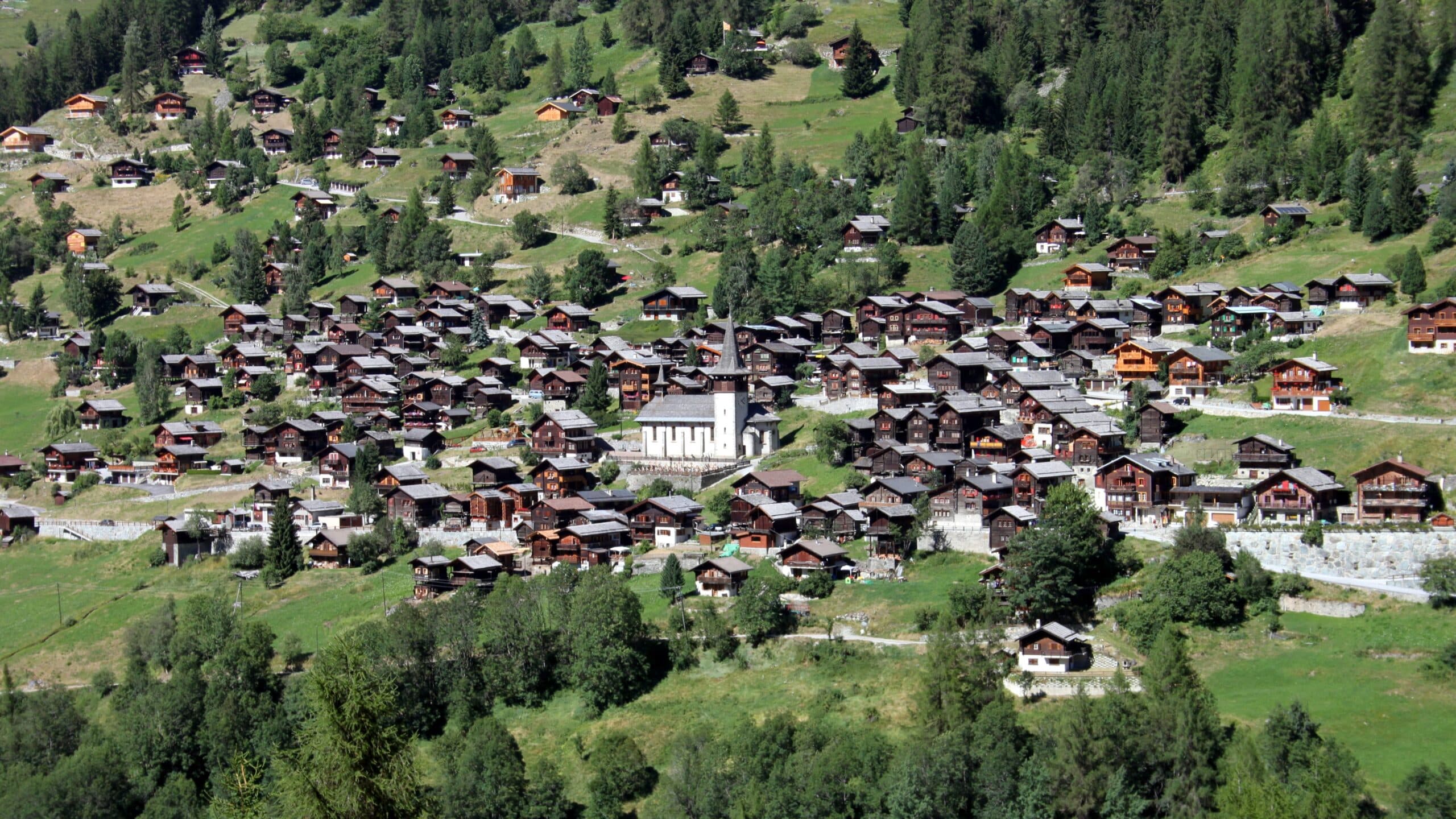 Village alpin suisse avec église et chalets sur pente verdoyante.