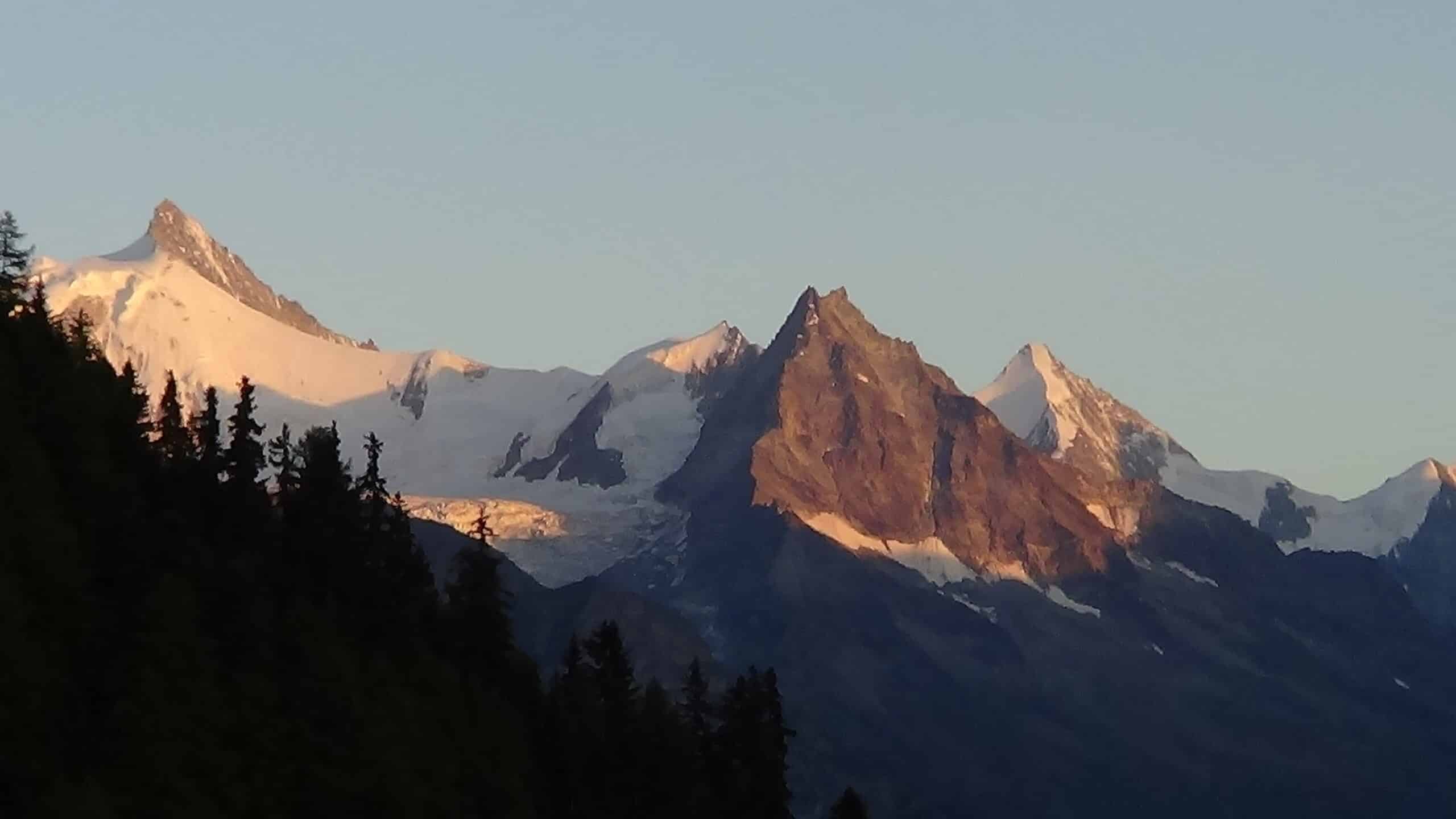 Montagnes enneigées éclairées par le soleil, avec forêts sombres.