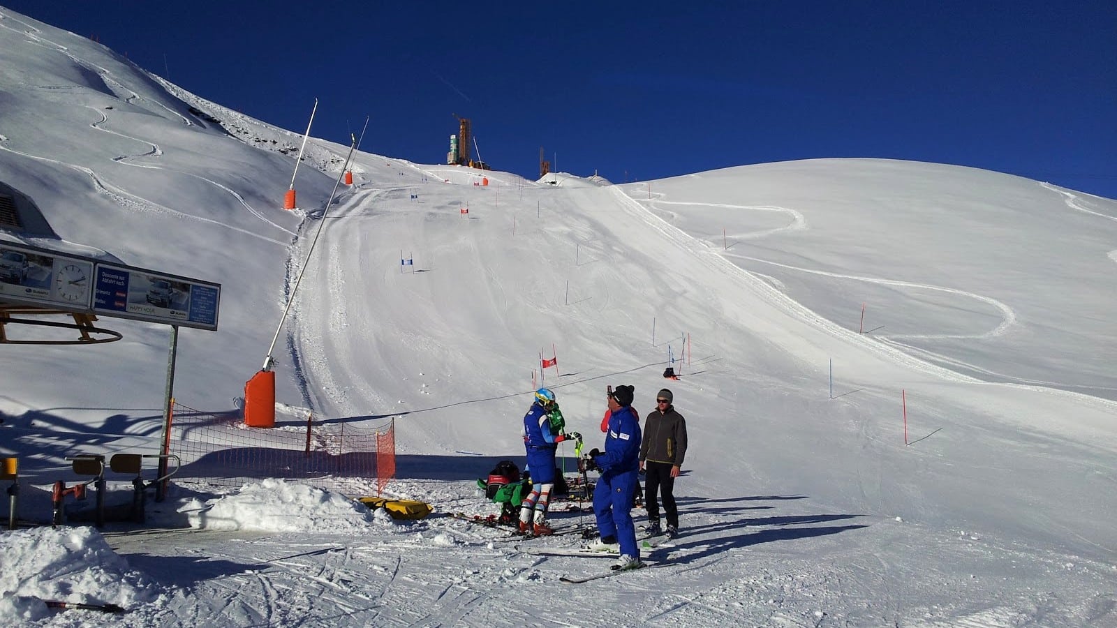 Piste de ski ensoleillée avec skieurs, télésiège et portes de slalom.