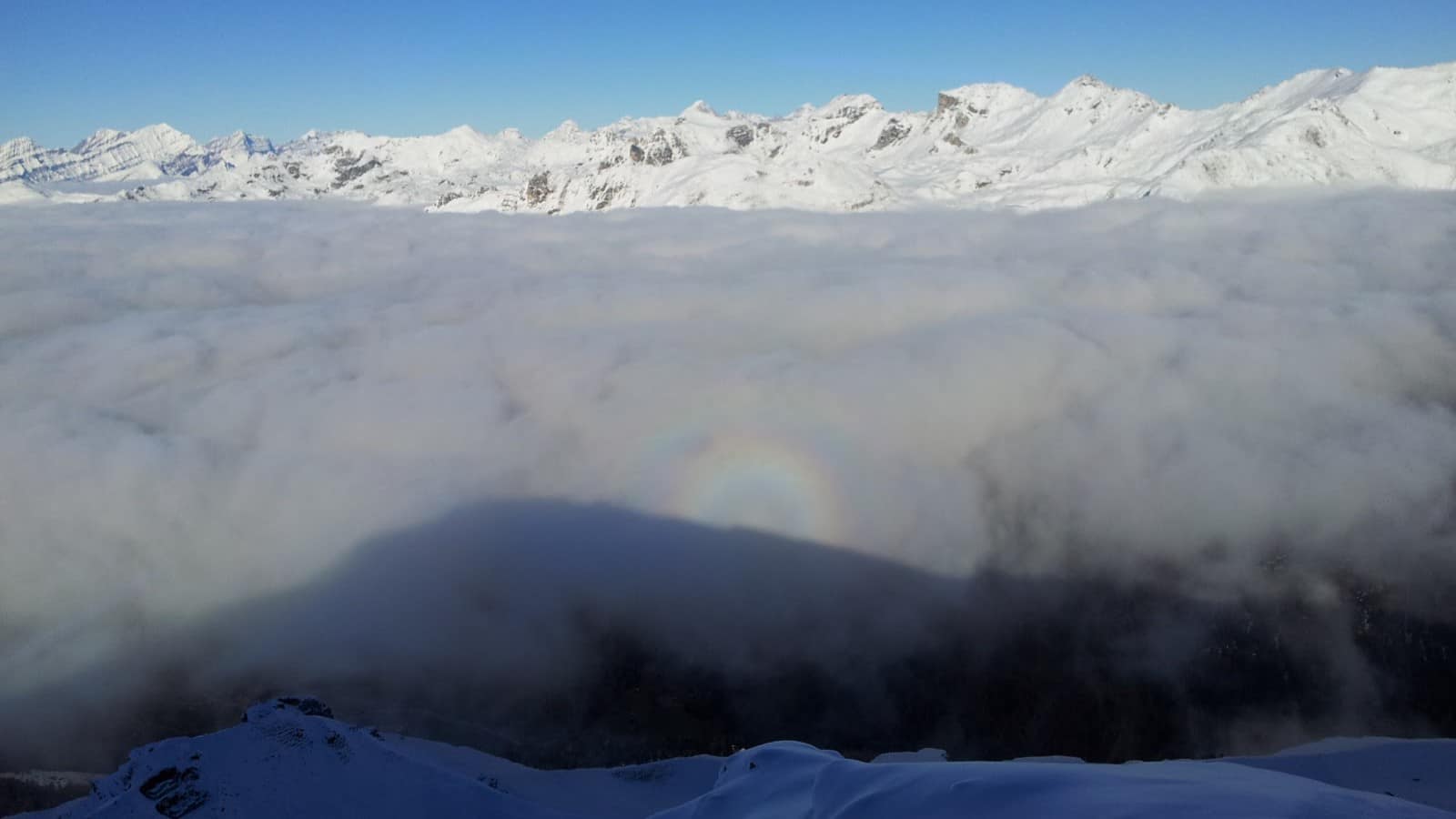 Mer de nuages, montagnes enneigées et spectre de Brocken sous ciel bleu.