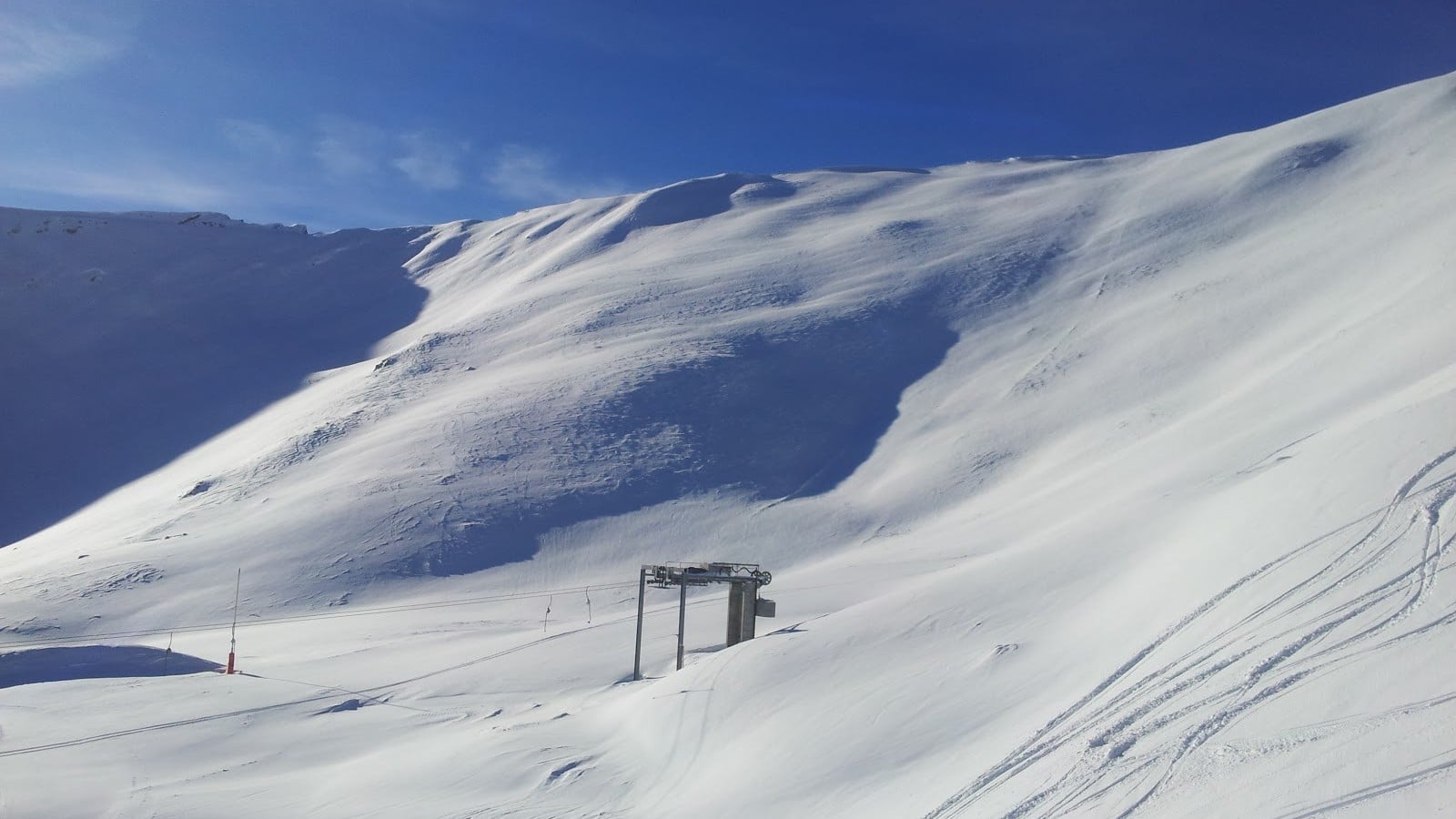 Piste de ski enneigée avec télésiège sous un ciel bleu.