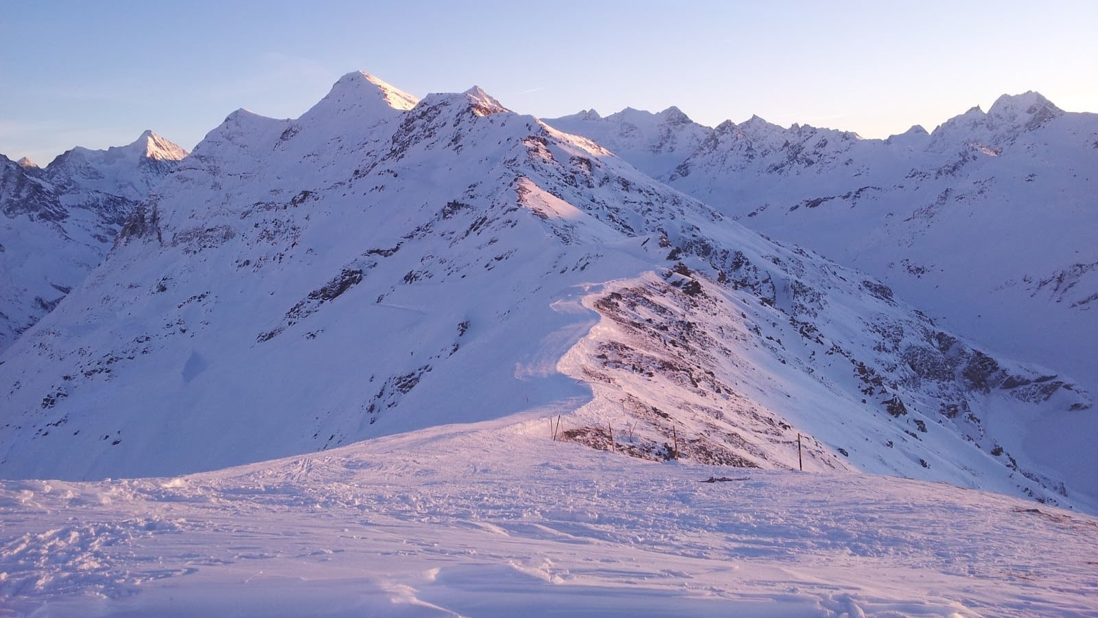 Chaîne de montagnes enneigées au soleil, crêtes et ciel bleu.