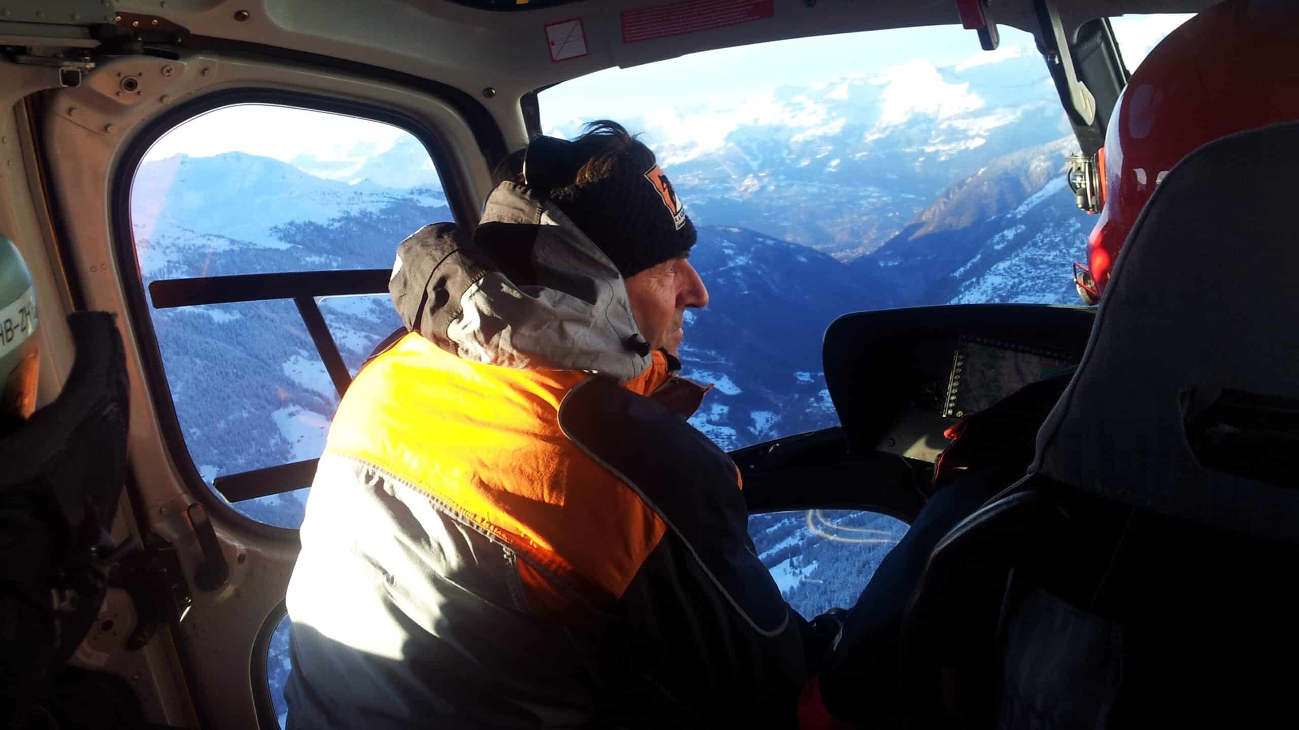 Homme en hélicoptère admirant les montagnes enneigées sous le soleil.