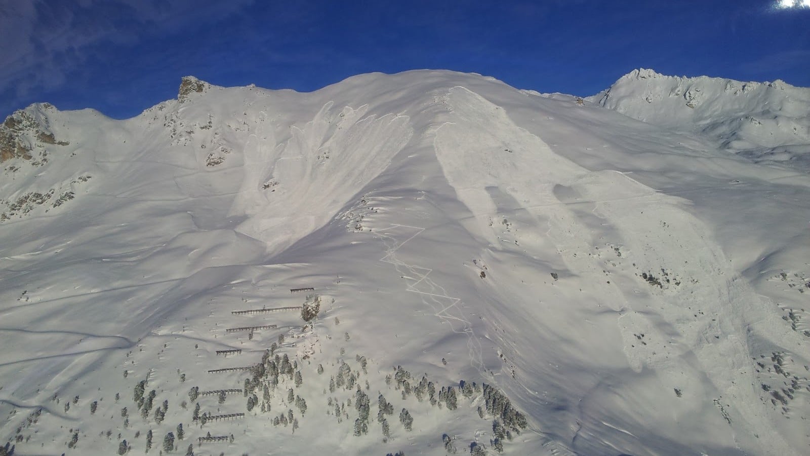 Montagnes enneigées sous ciel bleu, avec traces d'avalanches et paravalanches.