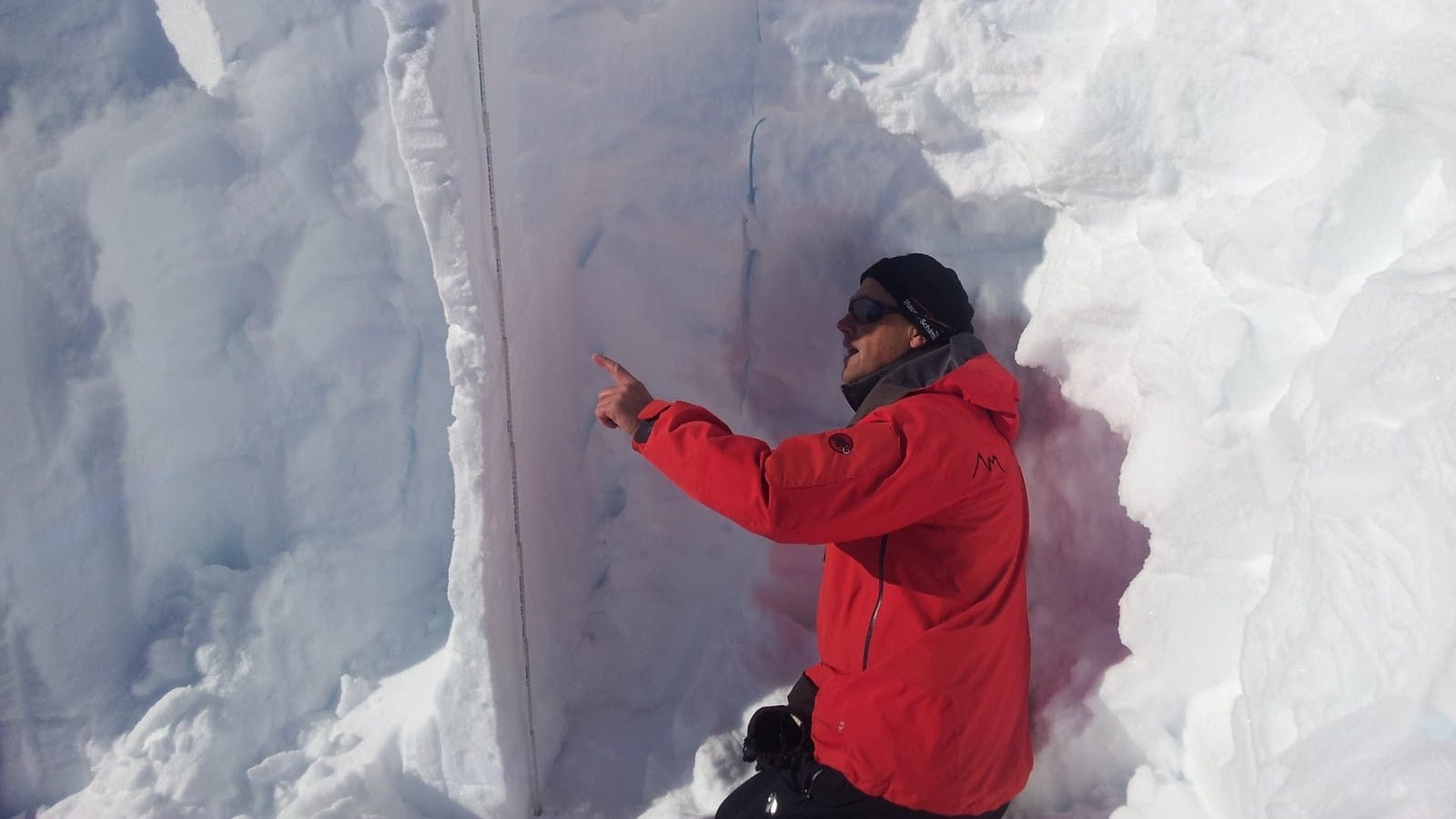 Homme en veste rouge examinant un profil de neige.