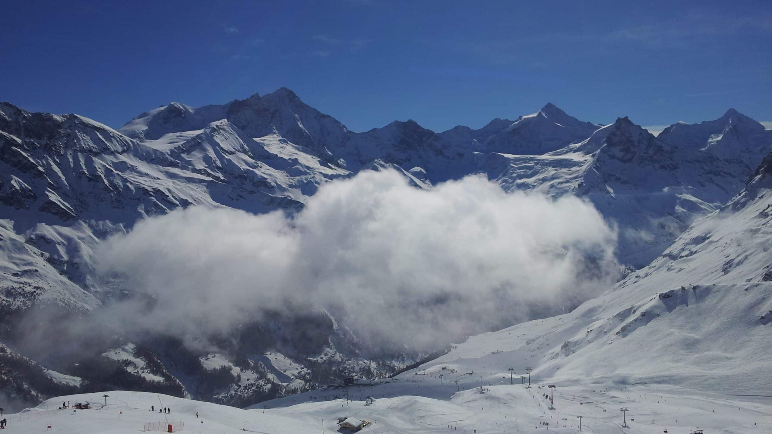Vue panoramique sur les montagnes enneigées, nuages et domaine skiable.