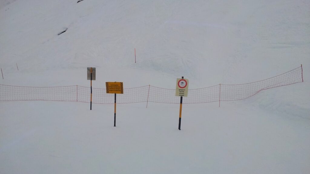 Barrières et panneaux de signalisation interdisant l'accès à la piste vers Zinal, sur un fond de neige.