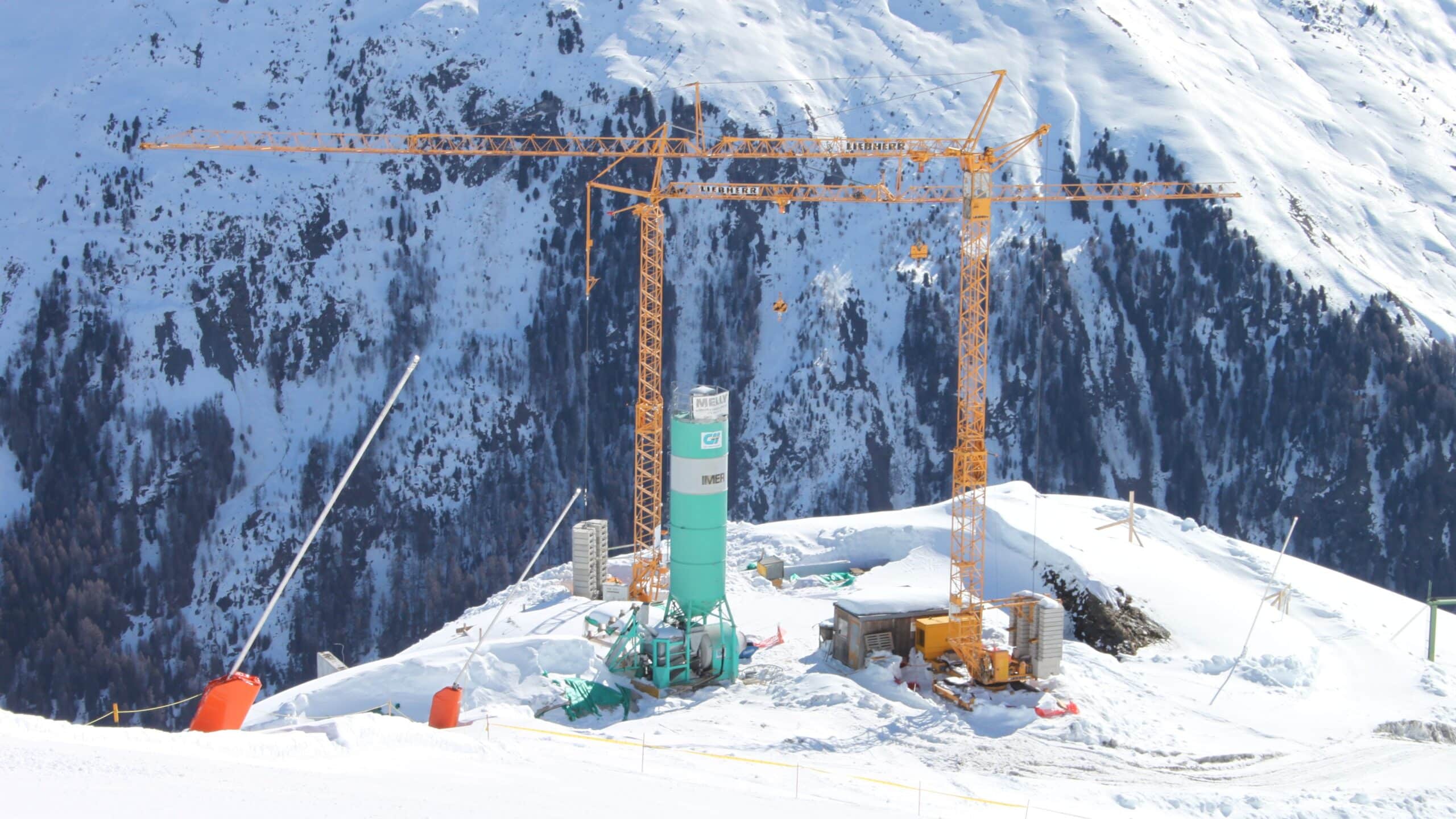 Site de construction avec grues Liebherr en montagne enneigée.