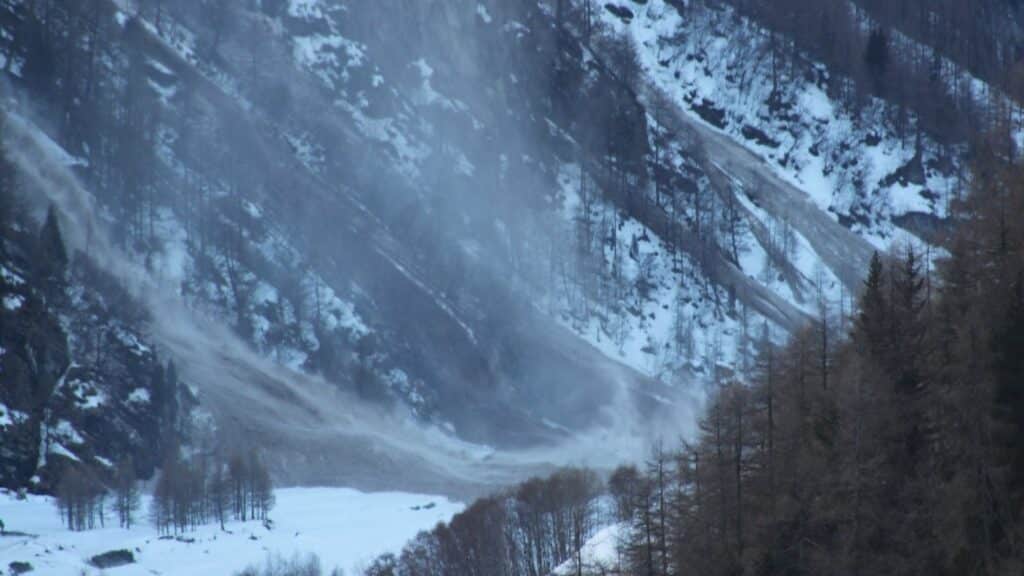 Avalanche in the Swiss Alps, showing snow and debris cascading down a mountainside.