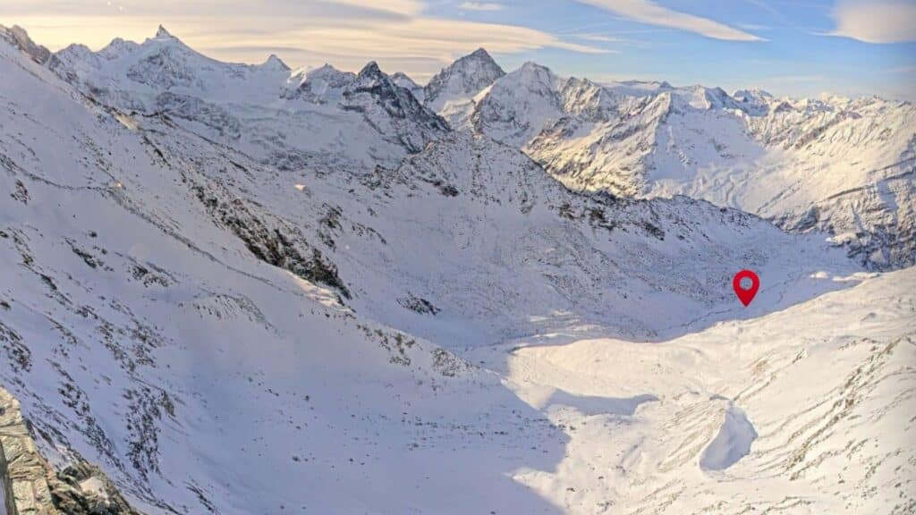 Vue panoramique des montagnes enneigées avec un point marqué sur la vallée, mettant en évidence le paysage alpin.