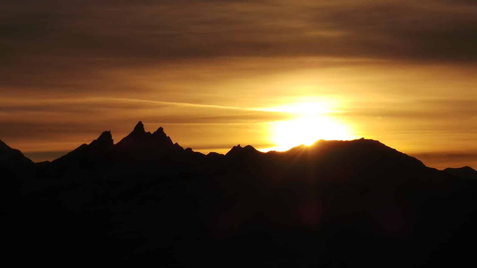 Coucher de soleil doré derrière des montagnes sombres.