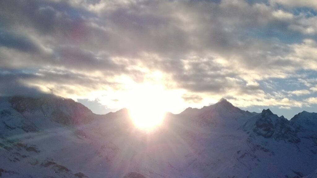 Le soleil levant entre les montagnes enneigées avec un ciel nuageux.