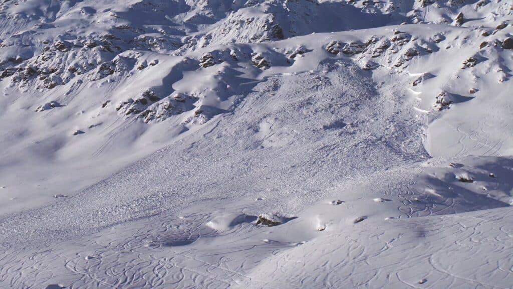 Vue d'une avalanche sur une pente enneigée, montrant des traces de ski sur la neige autour.