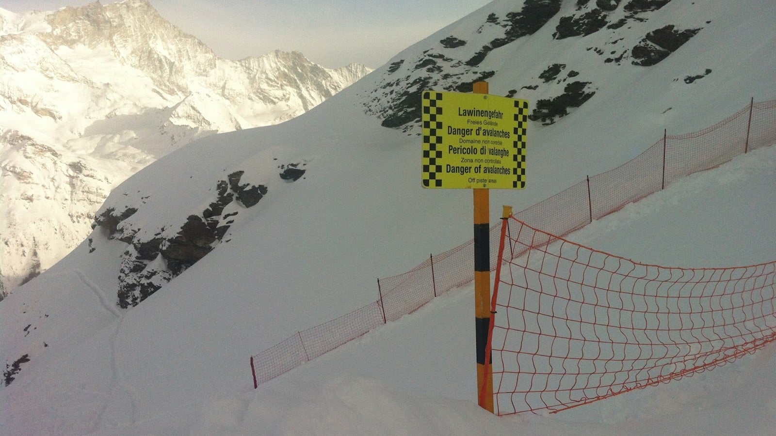 Panneau "Danger d'avalanches" et filet sur montagne enneigée.