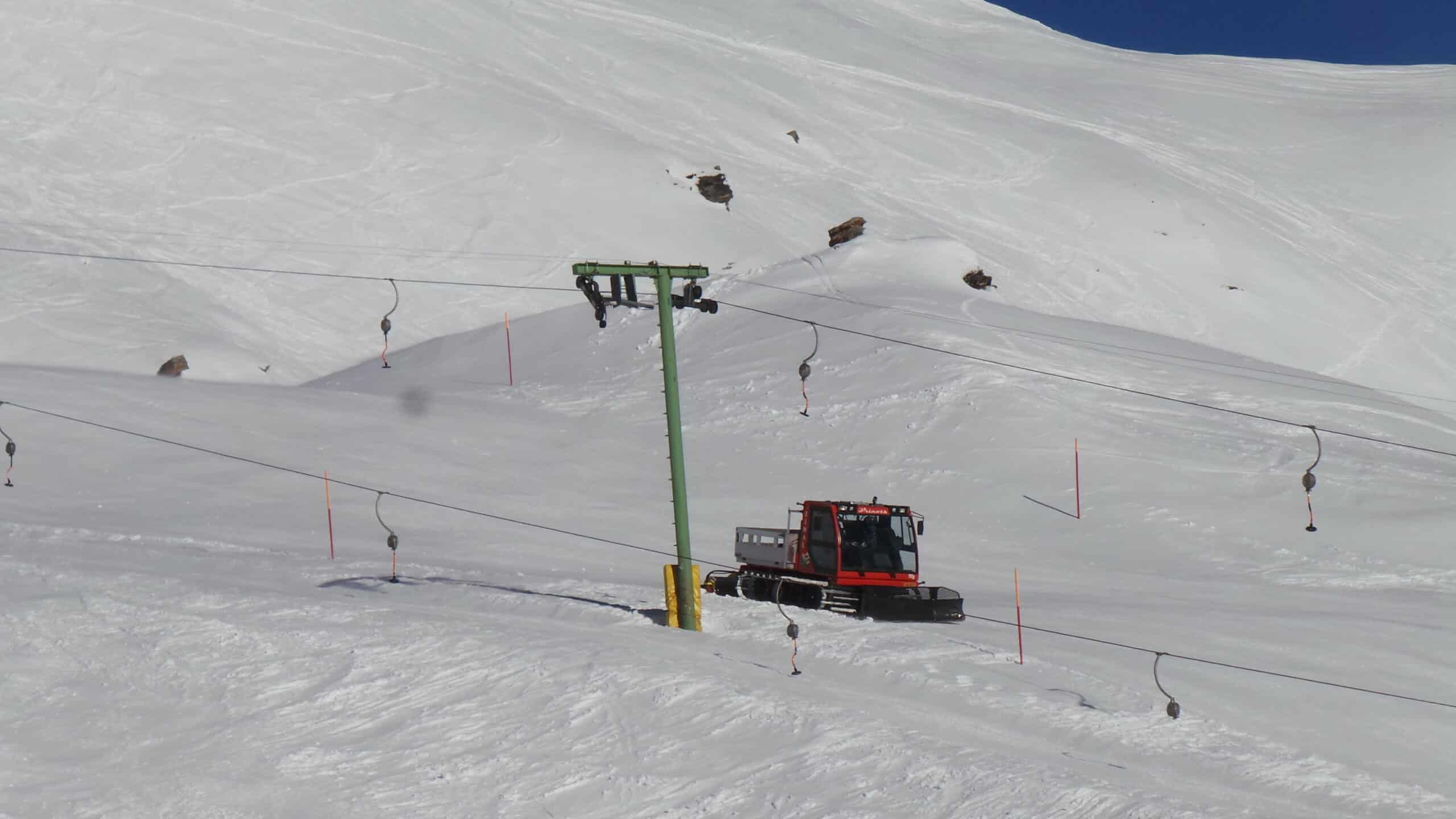 Dameuse rouge sur piste enneigée avec téléski.