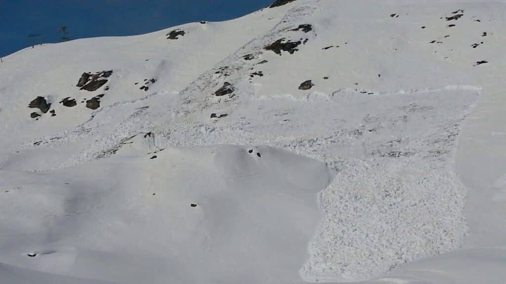 Vue d'une avalanche sur une pente enneigée, montrant une zone de neige fracturée et des plaques de neige accumulées.