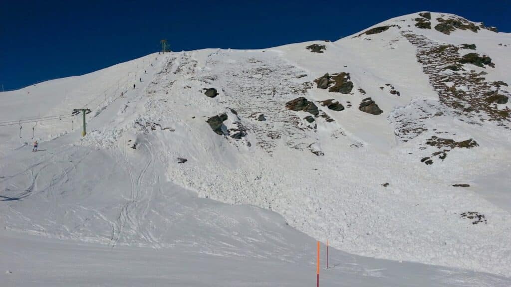 Vue d'une piste de ski avec un amas de neige à la suite d'une avalanche sous un ciel bleu.