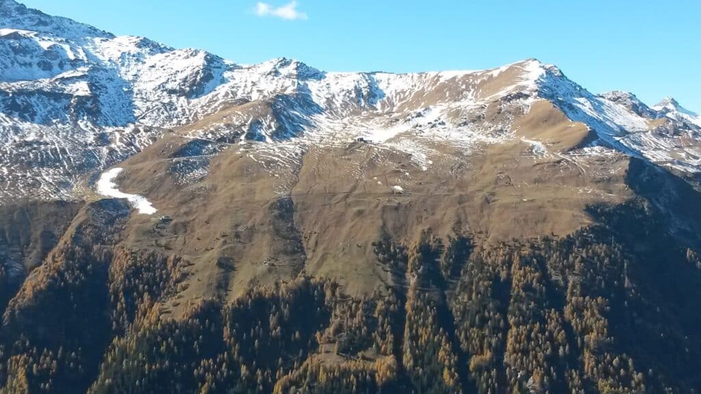 Vue des montagnes au-dessus de Lyrec, avec des sommets partiellement enneigés et des pentes verdoyantes sous un ciel clair.